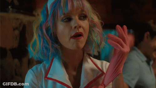 A Woman With Rainbow Hair Is Wearing A Nurse 'S Outfit And Holding A Pink Cotton Candy . GIF