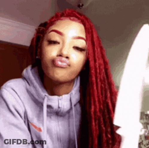 A Woman With Red Dreadlocks Is Wearing A Gray Hoodie And Making A Face . GIF