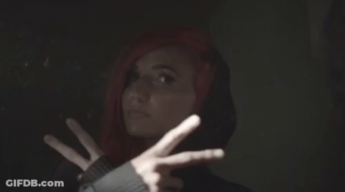 A Woman With Red Hair And A Black Hoodie Is Making A Peace Sign GIF