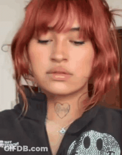 A Woman With Red Hair And A Heart Tattoo On Her Neck Is Wearing A Black Shirt With A Smiley Face On It . GIF