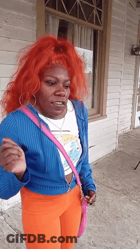 A Woman With Red Hair And A Pink Purse Stands In Front Of A Building GIF