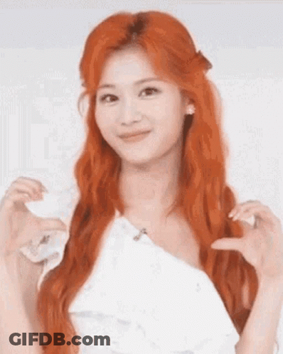 A Woman With Red Hair And A White Dress Is Making A Heart Shape With Her Hands . GIF
