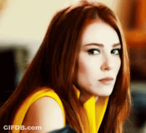 A Woman With Red Hair And A Yellow Shirt Is Looking At The Camera . GIF