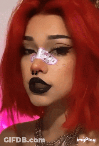 A Woman With Red Hair And Black Lips Is Wearing A Nose Ring And A Necklace . GIF
