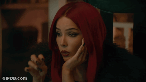 A Woman With Red Hair And Black Nails Holds Her Hand To Her Chin GIF