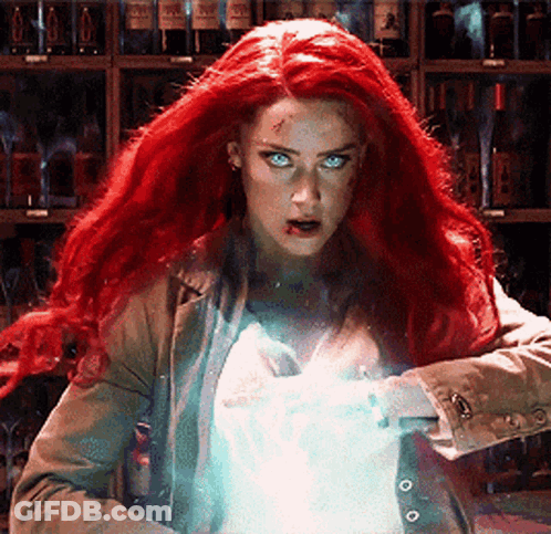 A Woman With Red Hair And Blue Eyes Is Standing In Front Of A Shelf Of Wine Bottles . GIF