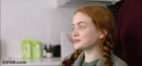 A Woman With Red Hair And Braids Is Sitting In A Chair In A Kitchen . GIF