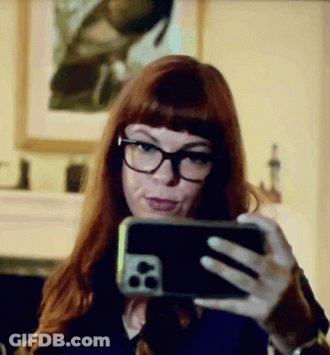A Woman With Red Hair And Glasses Is Taking A Selfie With Her Cell Phone GIF