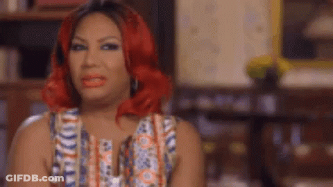 A Woman With Red Hair And Red Lipstick Is Sitting In A Chair In A Living Room . GIF