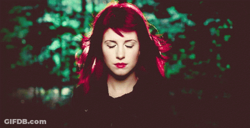 A Woman With Red Hair Has Her Eyes Closed In Front Of A Green Background GIF
