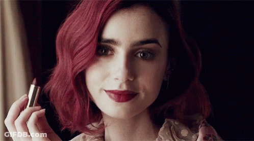 A Woman With Red Hair Holds A Lipstick In Her Hand GIF