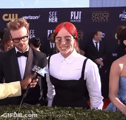 A Woman With Red Hair Is Being Interviewed By A Man In Front Of A Wall That Says Fiji Water GIF