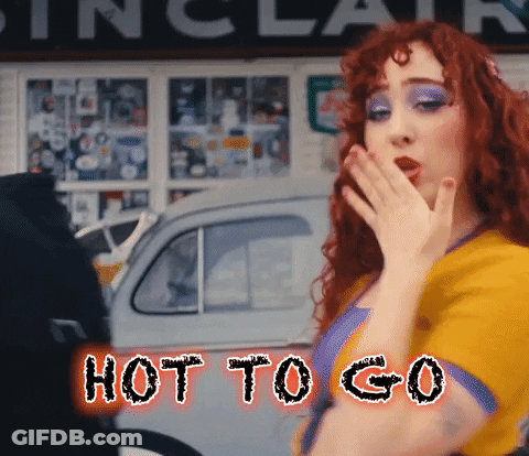 A Woman With Red Hair Is Covering Her Mouth With Her Hand And The Words Hot To Go Are Behind Her GIF