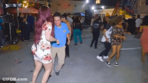 A Woman With Red Hair Is Dancing With A Man In A Blue Shirt In Front Of A Crowd Of People . GIF