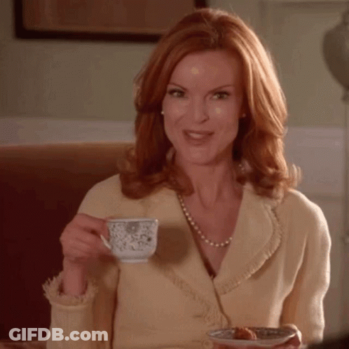 A Woman With Red Hair Is Drinking A Cup Of Tea And Holding A Plate Of Food GIF