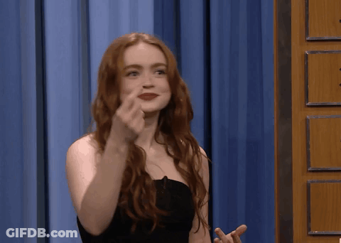 A Woman With Red Hair Is Giving The Middle Finger In Front Of A Blue Curtain GIF