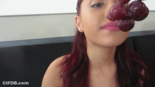 A Woman With Red Hair Is Holding A Bunch Of Grapes To Her Mouth GIF