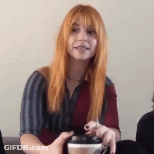 A Woman With Red Hair Is Holding A Cup Of Coffee In Her Hand . GIF