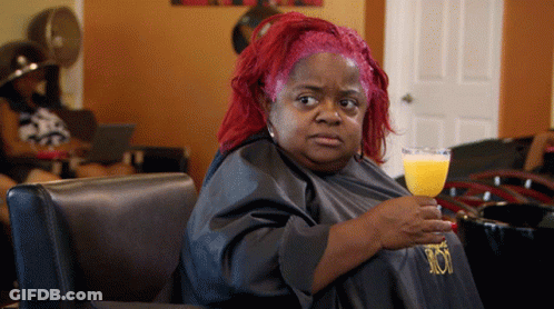 A Woman With Red Hair Is Holding A Glass Of Orange Juice In A Salon GIF