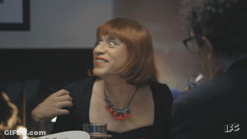 A Woman With Red Hair Is Holding A Glass Of Wine And Smiling GIF