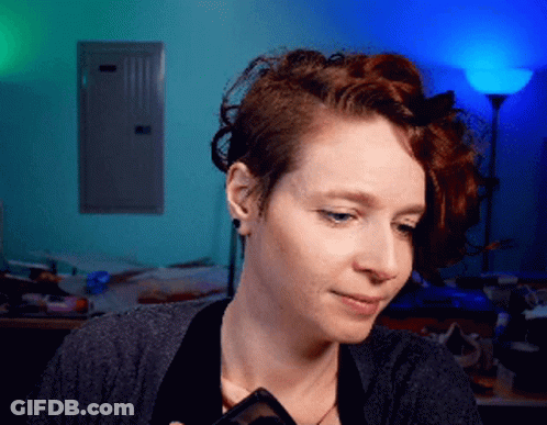 A Woman With Red Hair Is Holding A Phone In Her Hand GIF