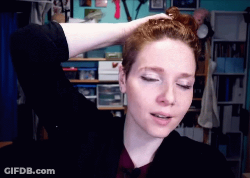 A Woman With Red Hair Is Holding Her Hair In A Messy Bun GIF