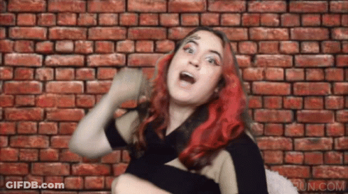 A Woman With Red Hair Is Making A Funny Face In Front Of A Brick Wall .. GIF