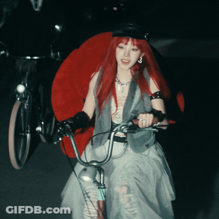 A Woman With Red Hair Is Riding A Bicycle In The Dark GIF