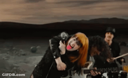 A Woman With Red Hair Is Singing Into A Microphone While A Man Plays Drums . GIF