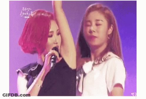 A Woman With Red Hair Is Singing Into A Microphone While Another Woman Holds Her Arm Up . GIF