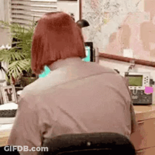A Woman With Red Hair Is Sitting At A Desk In Front Of A Map . GIF