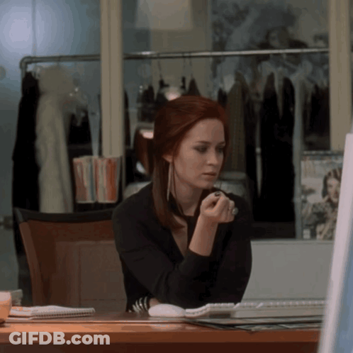 A Woman With Red Hair Is Sitting At A Desk Looking At A Computer Screen GIF