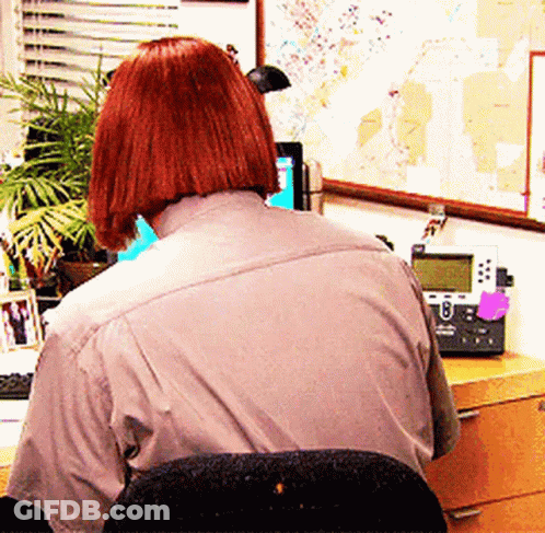 A Woman With Red Hair Is Sitting At A Desk With A Cisco Phone On It GIF