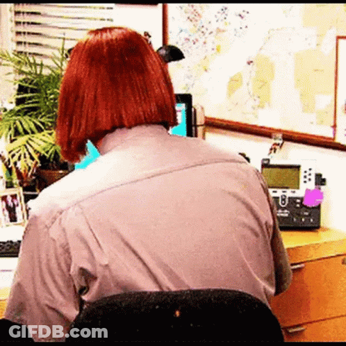 A Woman With Red Hair Is Sitting At A Desk With A Telephone And A Computer . GIF