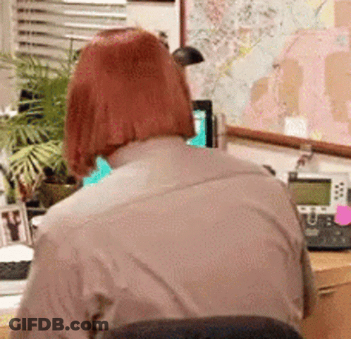 A Woman With Red Hair Is Sitting At A Desk With A Telephone And A Map On The Wall . GIF