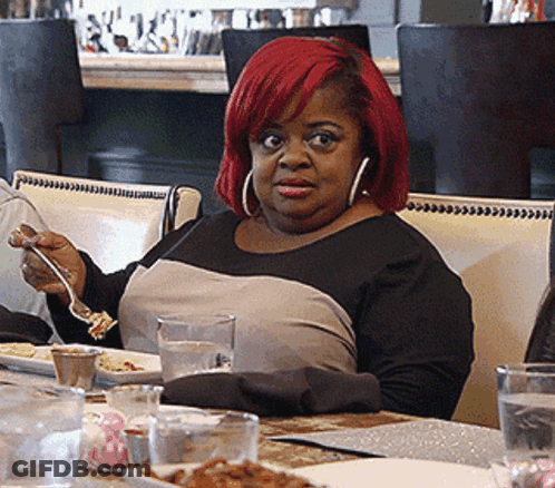 A Woman With Red Hair Is Sitting At A Table Eating GIF