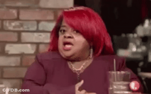 A Woman With Red Hair Is Sitting At A Table With A Glass Of Water In Front Of A Brick Wall . GIF