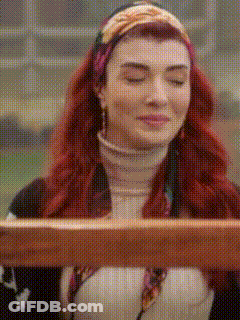 A Woman With Red Hair Is Sitting At A Table With Her Eyes Closed And Holding A Piece Of Wood . GIF