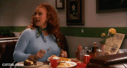 A Woman With Red Hair Is Sitting At A Table With Plates Of Food And A Menu GIF