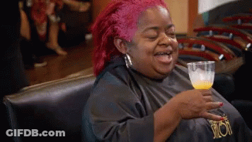 A Woman With Red Hair Is Sitting In A Chair Holding A Glass Of Orange Juice GIF
