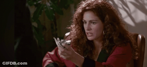 A Woman With Red Hair Is Sitting In A Chair Holding A Piece Of Paper In Her Hand . GIF