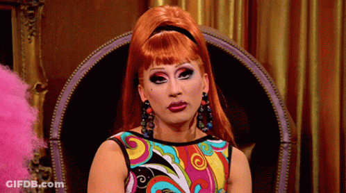 A Woman With Red Hair Is Sitting In A Chair Wearing A Colorful Dress . GIF