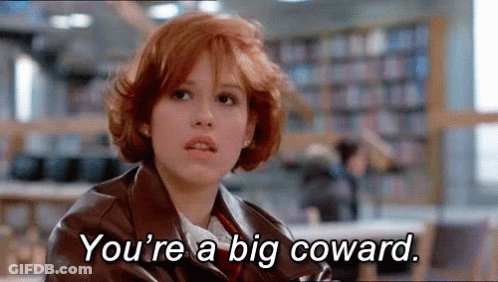A Woman With Red Hair Is Sitting In A Library With The Words `` You 'Re A Big Coward '' Written On Her Face . GIF