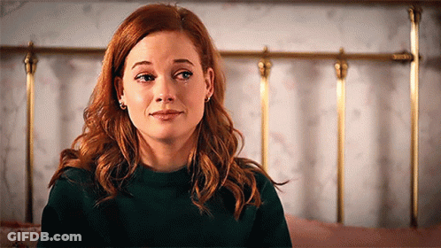 A Woman With Red Hair Is Sitting In Front Of A Bed . GIF