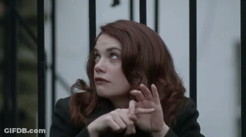 A Woman With Red Hair Is Sitting In Front Of A Metal Fence . GIF