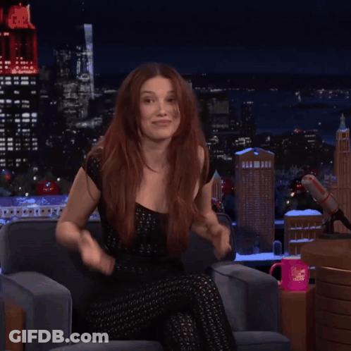A Woman With Red Hair Is Sitting In Front Of A Microphone With A Pink Mug That Says I Love You On It GIF