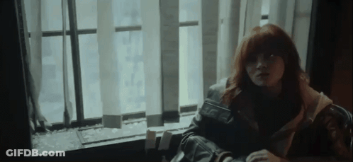 A Woman With Red Hair Is Sitting In Front Of A Window With Blinds . GIF