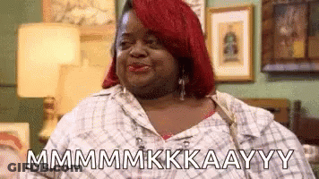 A Woman With Red Hair Is Sitting On A Couch In A Living Room And Making A Funny Face . GIF