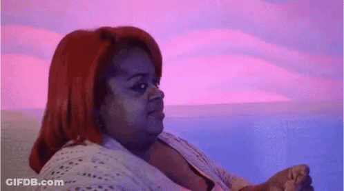 A Woman With Red Hair Is Sitting On A Couch In Front Of A Pink And Blue Background . GIF