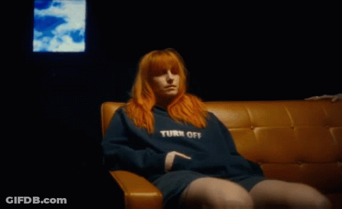 A Woman With Red Hair Is Sitting On A Couch In Front Of A Television . GIF